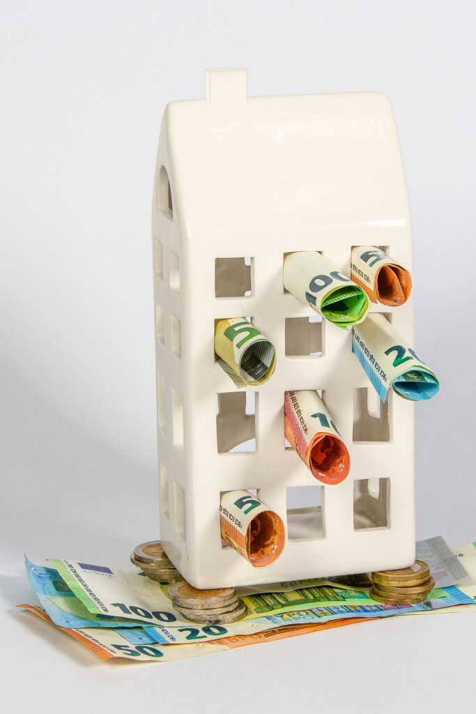 Figurine de maison entourée de billets et de pièces, illustrant le revenu d'un mandataire immobilier